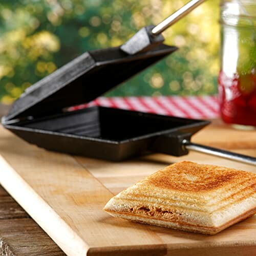 Cast iron sandwich maker with toasted sandwich on wooden board.