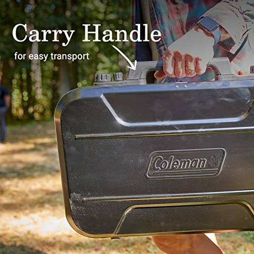 Person carrying Coleman stove with handle for easy transport.