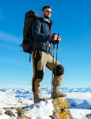 A hiker in winter gear standing on a snowy mountain peak.