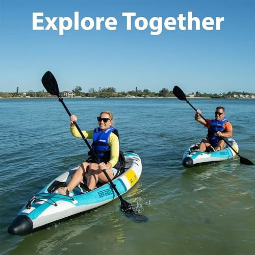 Two people kayaking on a lake with blue skies.