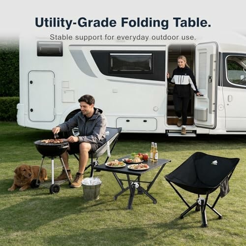 People enjoying a barbecue near a camper with folding table and chairs.