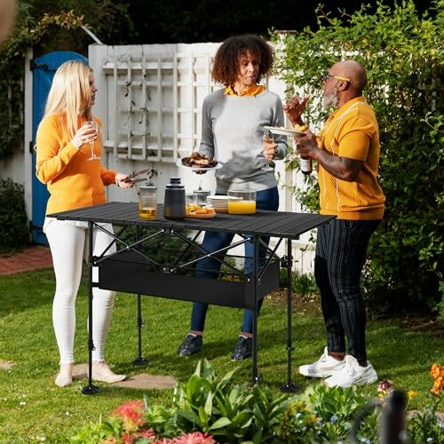 Three people talking and enjoying drinks around a portable outdoor table in a garden.