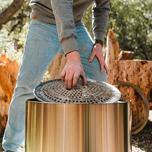 Person placing lid on a metal fire pit outdoors.