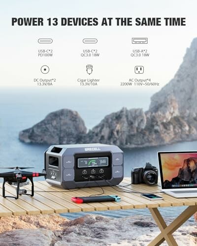 Portable power station on table charging a drone, camera, and laptop outdoors.