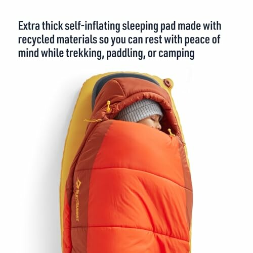 Person in orange sleeping bag on a self-inflating sleeping pad.